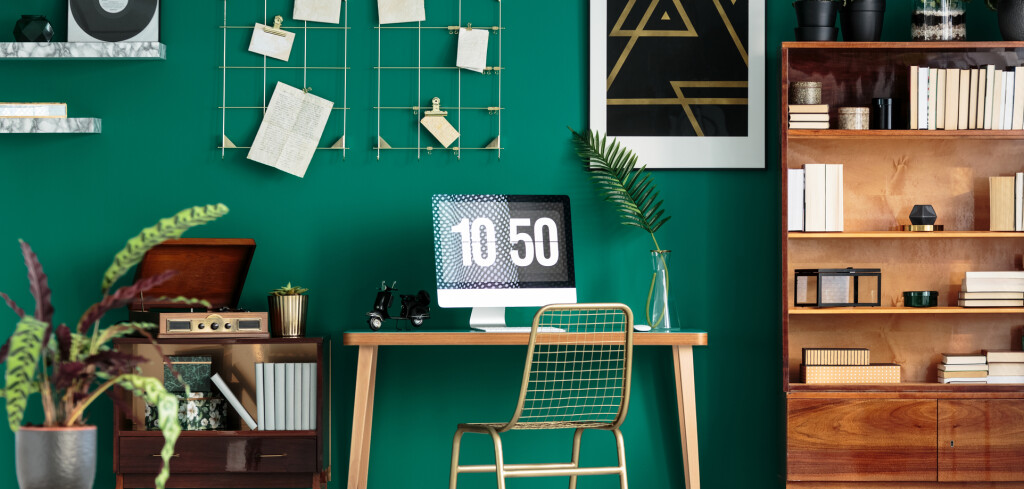 Home office and study corner with wooden desk and computer in green room interior with plants and poster