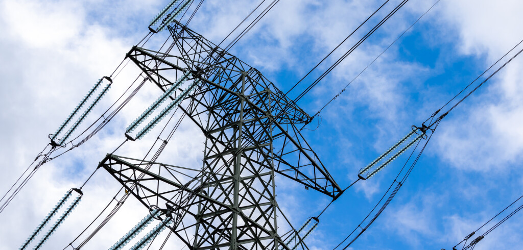 High-voltage pylon against a blue sky with a slight cloud cover. High voltage transmission lines silhouette