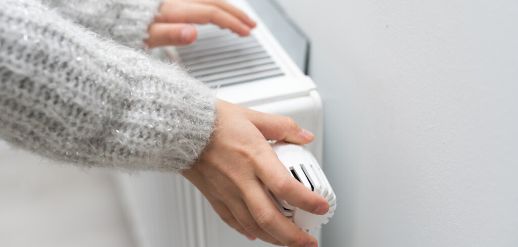 The child's hands warm their hands near the heating radiator. Saving gas in the heating season