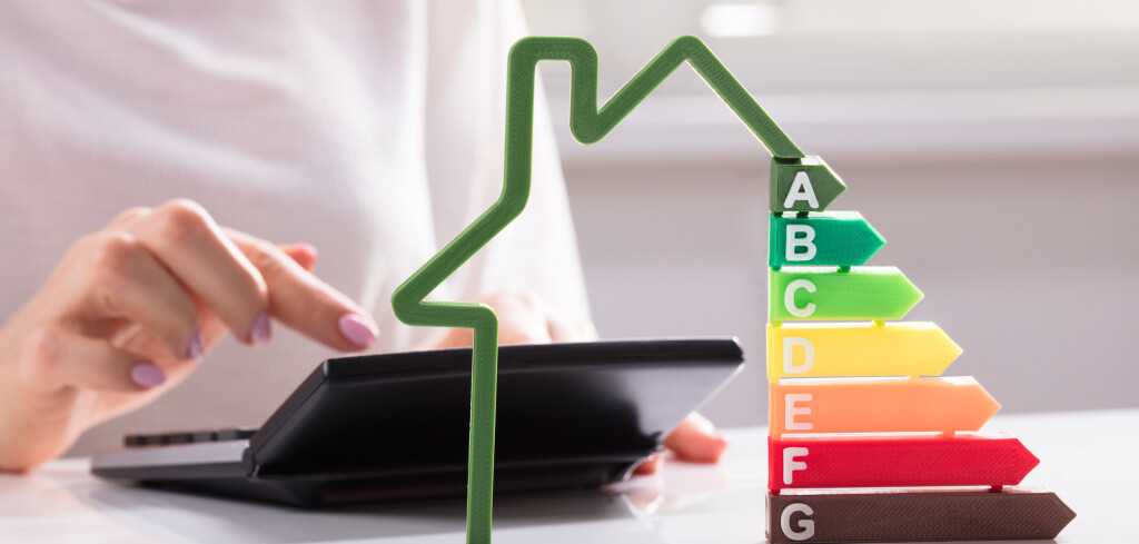 Close-up Of A House Showing Energy Efficiency Rate In Front Of Businesswoman Using Calculator