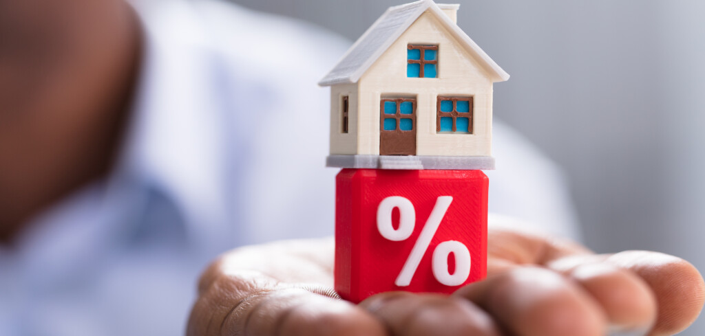 Close-up Of A Person's Hand Holding Miniature House On Red Percentage Block