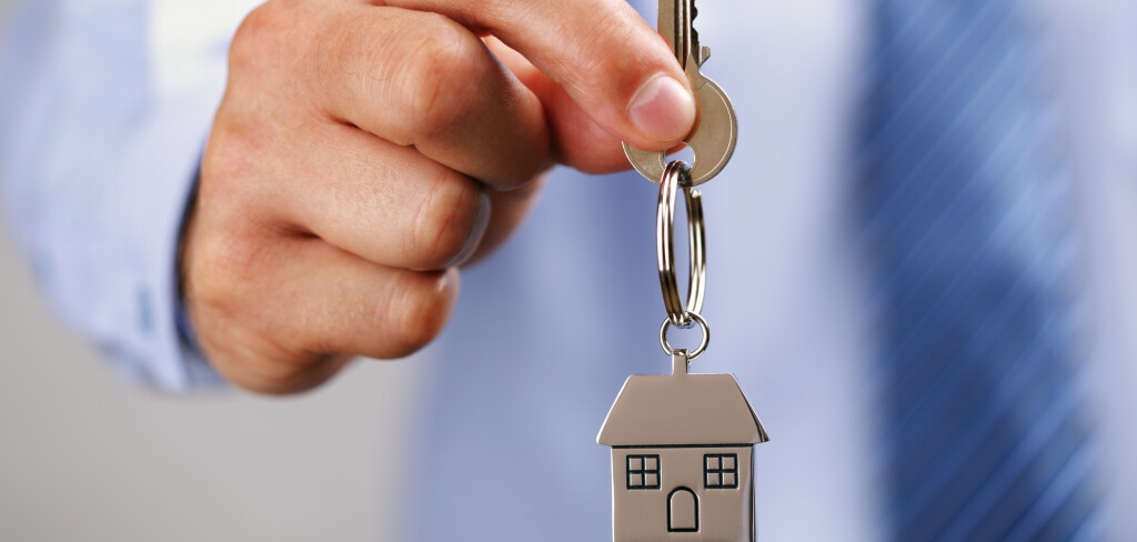 Holding out house keys on a  house shaped keychain