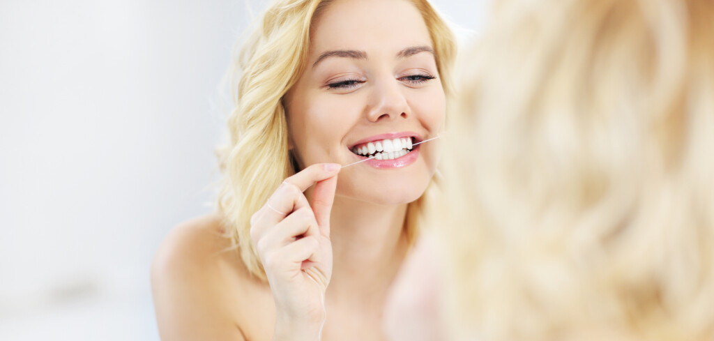 A picture of a young happy woman using dental floss in the bathroom