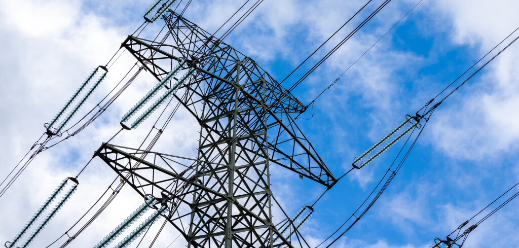 High-voltage pylon against a blue sky with a slight cloud cover. High voltage transmission lines silhouette